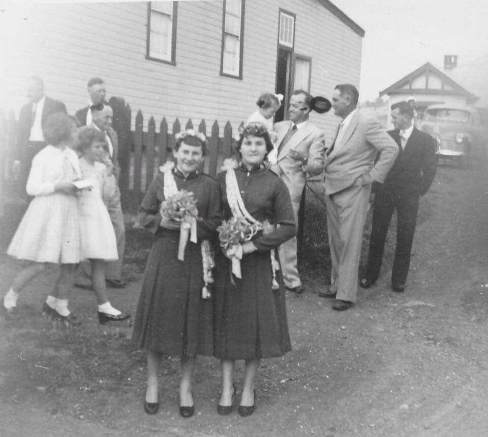 Two young women in formal dresses with floral sashes, mid-1950s