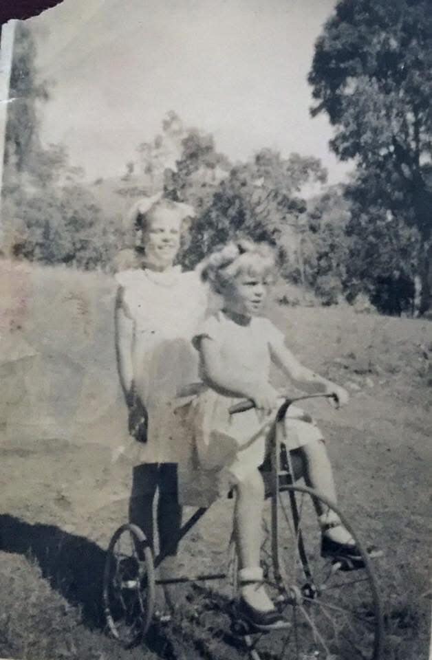 Two small girls in summer dresses, one seated on a tricycle, mid-twentieth century