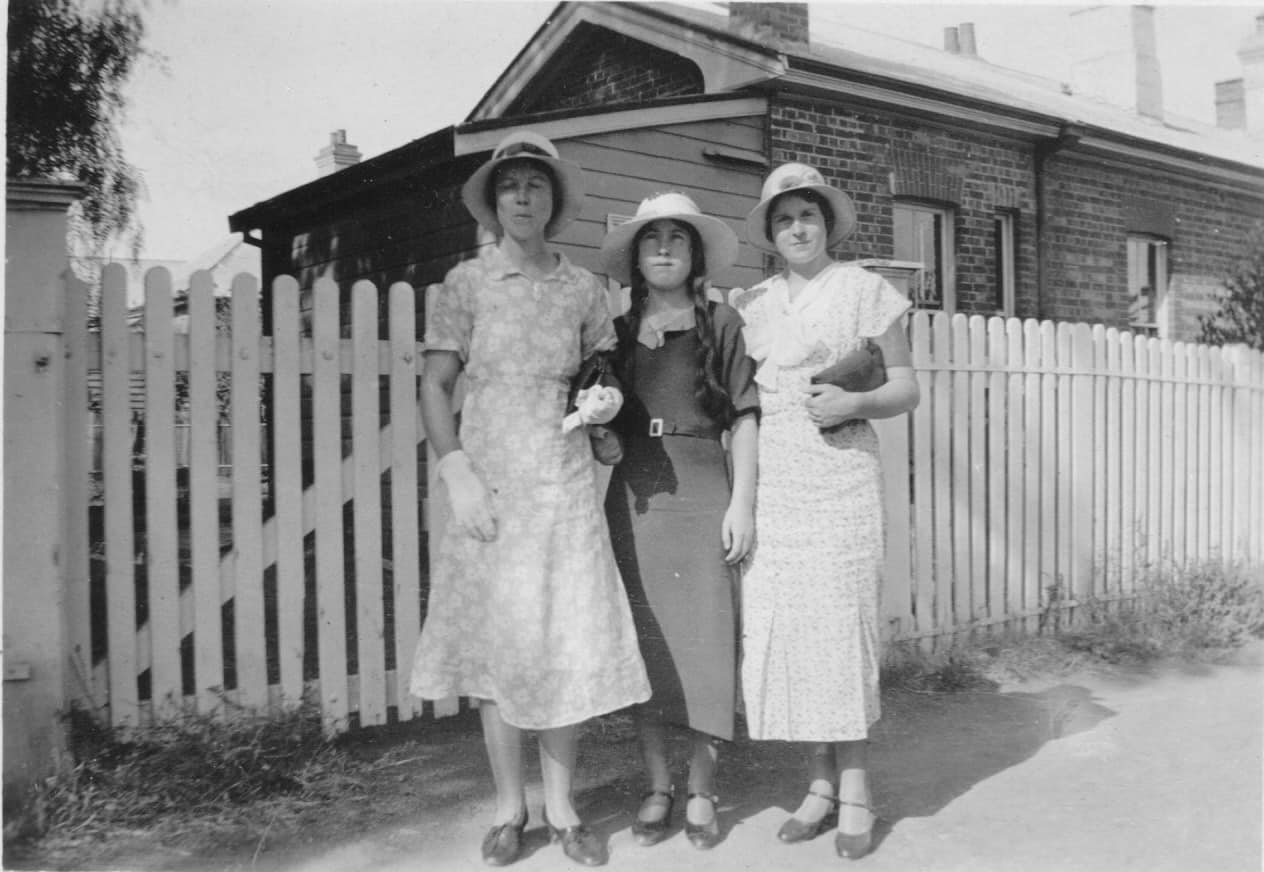 Three women in 1930s dresses outside a Federation cottage